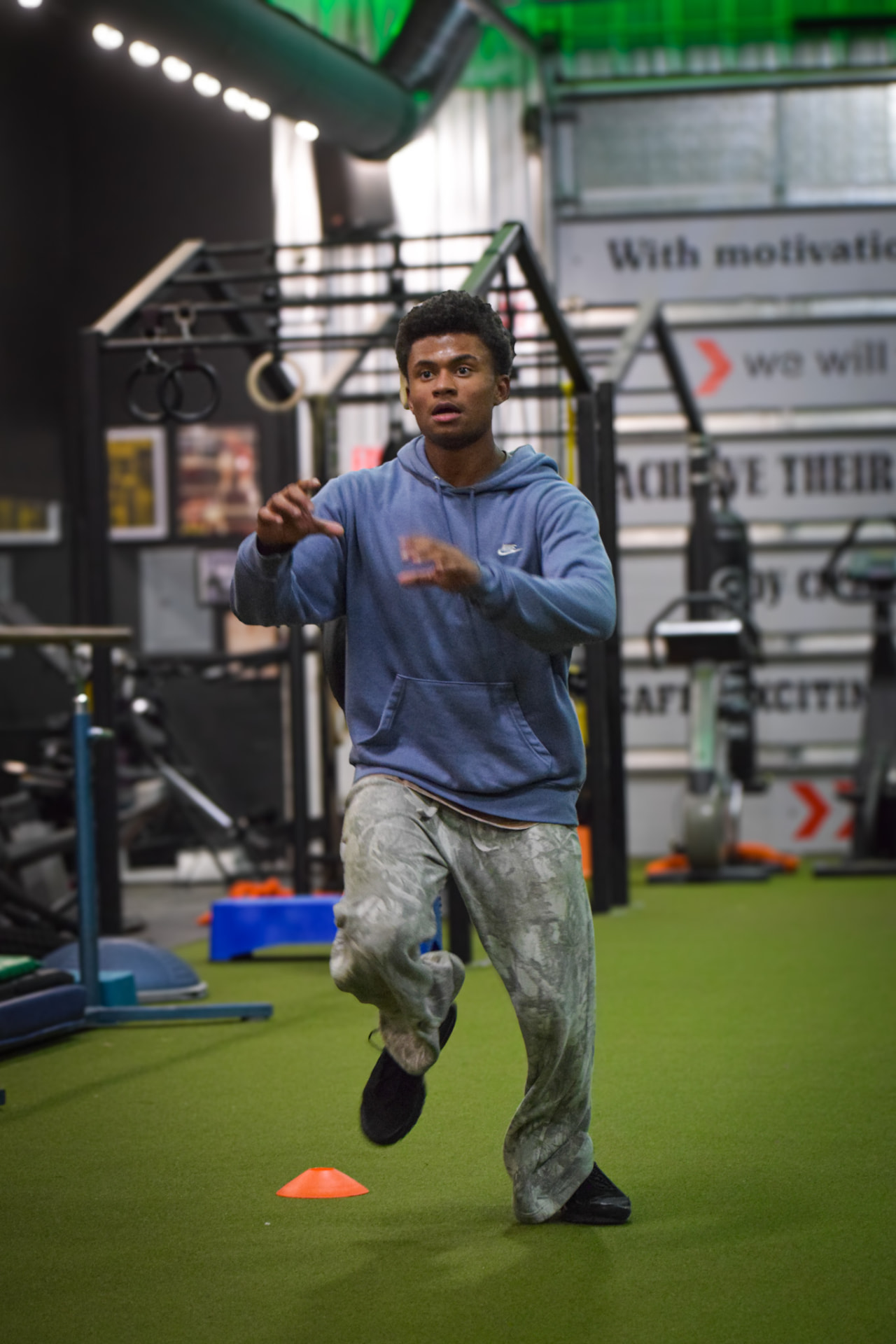 Athlete in a blue hoodie training footwork over a cone